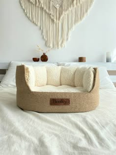 a dog bed that is on top of a white bed with fringes hanging above it