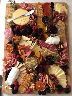 an assortment of cheeses, meats and fruit on a cutting board with crackers