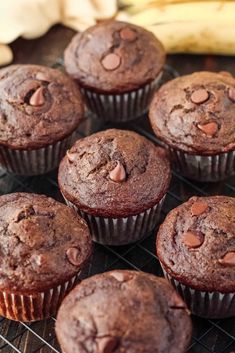 chocolate muffins cooling on a wire rack with bananas in the backround