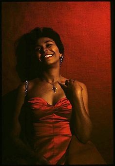 a woman in a red dress smiling with her hands on her chest and wearing earrings