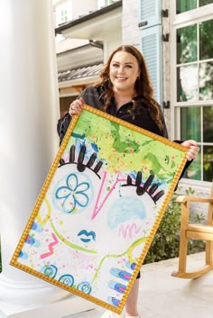 a woman is holding up a large painting