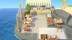 a woman sitting at a table in front of a restaurant next to the ocean with food on it