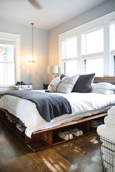 a bed sitting in the middle of a bedroom next to two windows with shoes on them