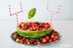 a watermelon bowl filled with fruit and two straws sticking out of it