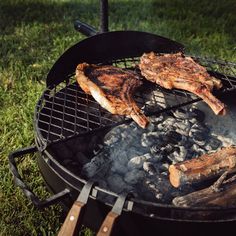 two pieces of meat are being cooked on a grill in the grass with tongs