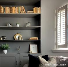 a living room filled with furniture and bookshelves next to a window covered in shutters