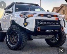 the front end of a white toyota 4x4 with black tires and lights on