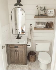 a white toilet sitting next to a sink in a bathroom under a mirror and wooden shelves