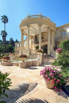 a large white house with lots of flowers in the front yard and stairs leading up to it