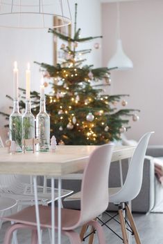 a dining room table with chairs and a christmas tree in the background, surrounded by candles