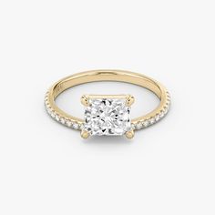 a gold engagement ring with a princess cut diamond in the center and pave set shoulders