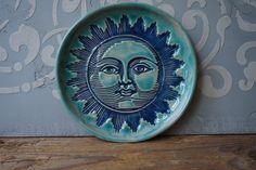 a blue plate with a sun face on it sitting on a wooden table next to a wall