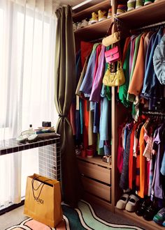 a closet filled with lots of colorful clothes and handbags on top of shelves next to a window