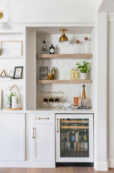 a kitchen with white cabinets and shelves filled with bottles, wine glasses and other items