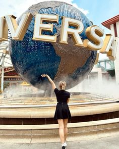 a woman is standing in front of the universal studios sign with her arms raised up