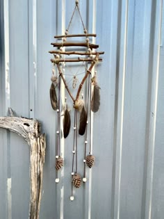 an old wind chime hanging on the side of a building with pine cones and feathers