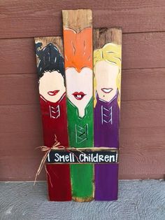 three painted wooden skis with the words i smell children written on one side and an image of two women's faces in different colors