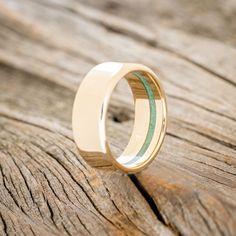 a gold ring with green and white stripes on the inside, sitting on a piece of wood