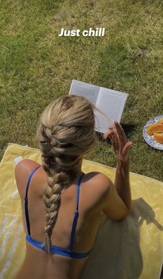 a woman sitting on top of a towel next to an open book and oranges