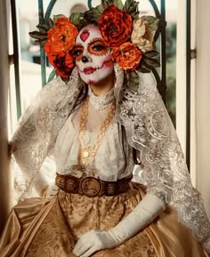 a woman with makeup and flowers on her head sitting in front of a window wearing a costume