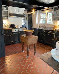 a large kitchen with black cabinets and red tile flooring, an island in the middle