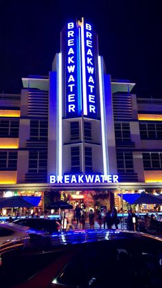 the front of a hotel at night with cars parked in front and people walking around