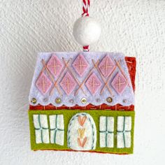 a felt house ornament hanging on a wall with a candy cane in it