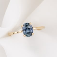 a blue diamond ring sitting on top of a white cloth with a yellow gold band