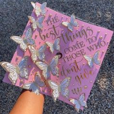 a hand holding a purple graduation cap with butterflies on it that says, the best things come to those who don't give up