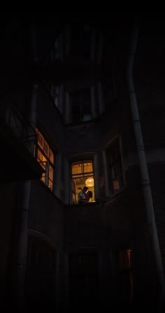 two people standing in the window of an old building at night with their lights on