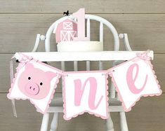 a pink and white baby shower banner with a pig on it's head hanging from a chair