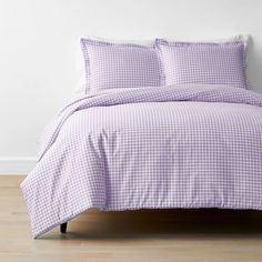 a purple and white checkered comforter set on a wooden floor in front of a white wall