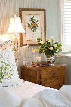 a bedroom with white bedding and flowers on the nightstand