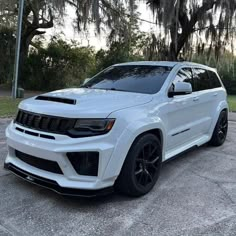 the white jeep is parked in front of some trees