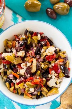 a white bowl filled with lots of different types of food next to olives and peppers