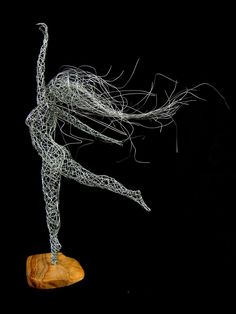 a wire sculpture of a woman on a wooden base with her arms in the air