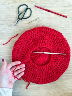 someone is crocheting a red hat with scissors and yarn