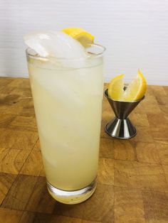 a glass filled with ice and lemon wedges on top of a wooden table next to a metal strainer