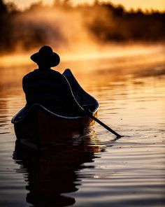 a person in a canoe paddling on the water at sunset or dawn with mist rising from behind