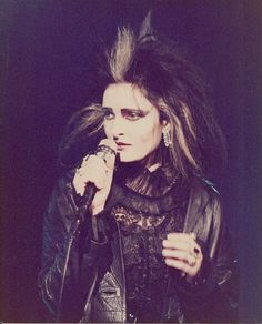 a woman with long hair holding a microphone in her hand and wearing black leather jacket