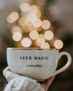 a person holding a cup with the words seek magic everyday written on it in front of a christmas tree