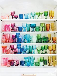 a shelf filled with lots of different colored glasses on top of each other in front of a white wall