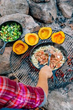 a person cooking food on top of a grill next to some vegetables and eggs in skillets