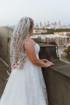 a woman in a wedding dress standing on top of a roof looking at the city