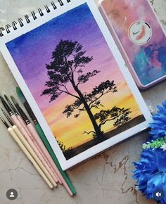 a notebook with an image of a tree on it next to some paintbrushes