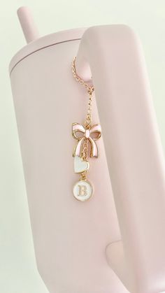 a pink cup with a gold bow and initial charm hanging from it's side