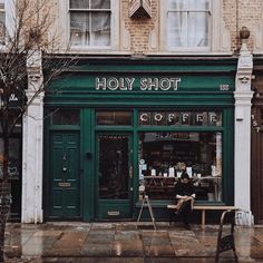 a man sitting at a table in front of a coffee shop with green doors and windows