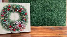 a christmas wreath painted on a canvas next to a wall with fake greenery behind it