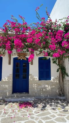 a white building with blue doors and pink flowers growing on it's side wall