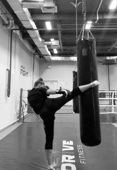 a woman kicking a punching bag with her leg in an empty boxing ring, black and white photograph